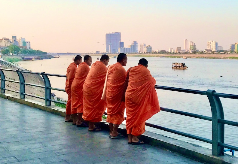 Young monks on a twilight stroll pause to ponder passing boats on the Tonlé Sap river in central Phnom Penh. 