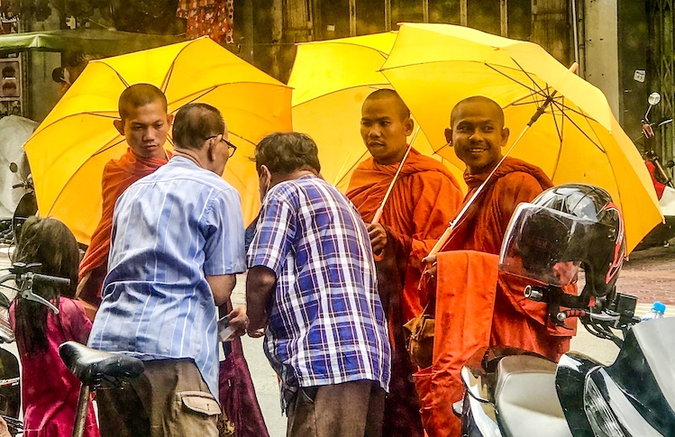 A trio of monks accept daily alms for prayers delivered to downtown merchants. Traditional Theravada Buddhism continues to be practiced throughout Cambodia.