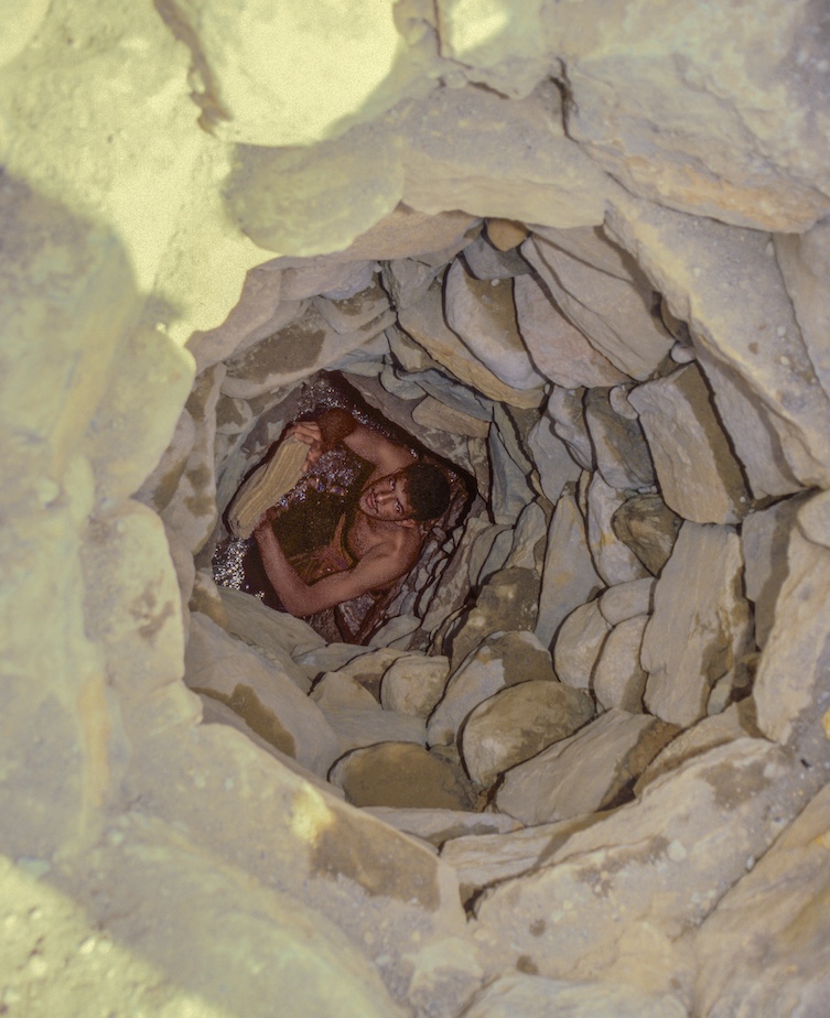 Young man removing dirt and salt deposits from an underground water channel, or falaj, in Oman's Wadi Bani Kharus.