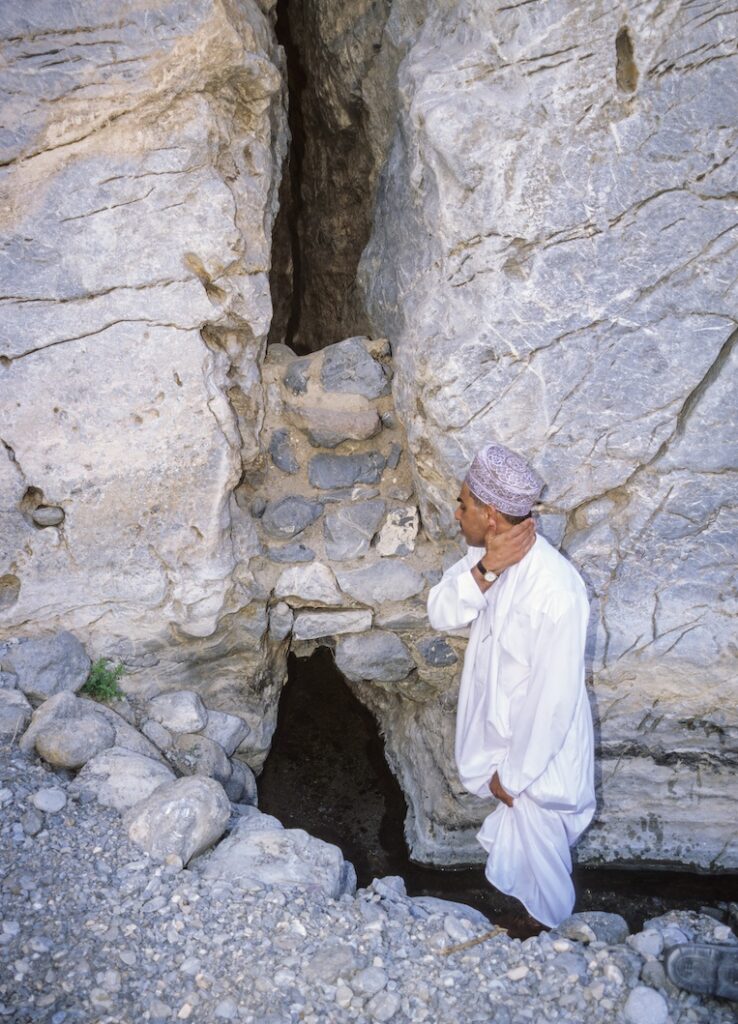 An Omani refreshes himself with cool water issuing from a cleft in the rock in the narrow mountain valley of Wadi Bani Kharus. Water from such springs flows by gravity through a series of canals and channels, called aflaj (singular, falaj), to terraced gardens farther down the mountain valley. 