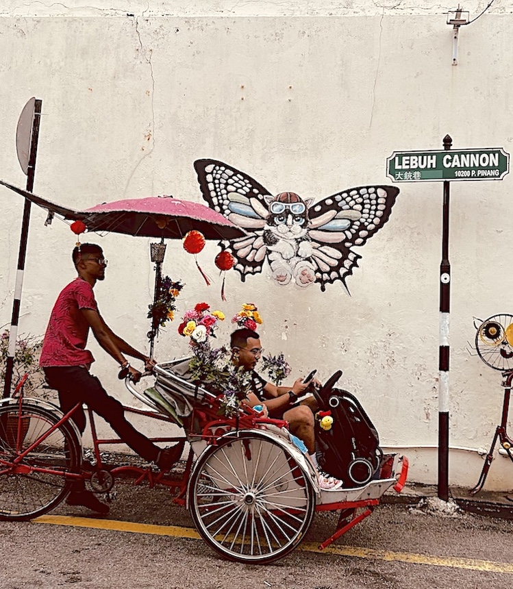 Trishaw driver pauses next to a playful mural in downtown George Town, capital of Penang.